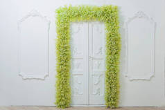 春天的装饰。白色的墙壁。墙上挂着漂亮的灰泥。绿色和白色的花的拱门。照片区。门口的装饰有鲜花。白色宝宝的呼吸.