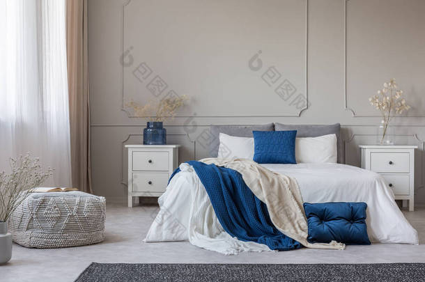 蓝色枕头和毯子在宽敞的卧室内部的白色床上，在空灰色墙壁上复制空间