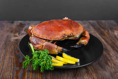 黑盘上的煮熟的螃蟹配以新鲜的柠檬和欧芹，木制背景，顶视图.