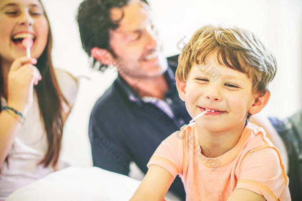 快乐的家庭一起在家里的床上快乐-一个孩子的肖像在客厅里与他的父亲和妹妹一起笑-团结, 家庭和爱的概念