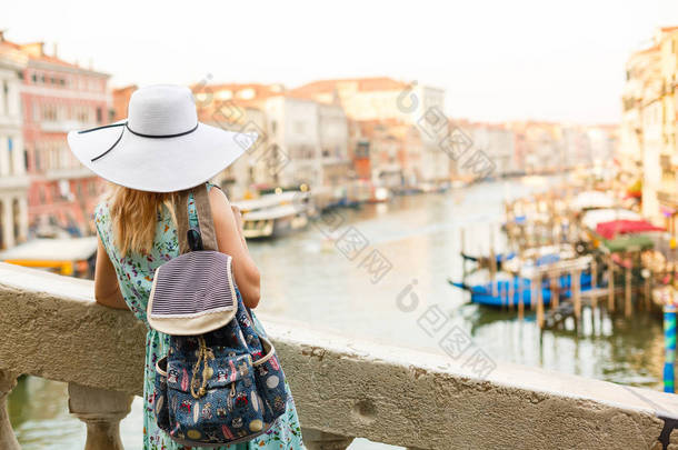 在意大利威尼斯，穿着蓝色衣服、头戴蓝色帽子的女人在大街上欢快而快乐地走在后视镜下，展示着太阳衣的背面.