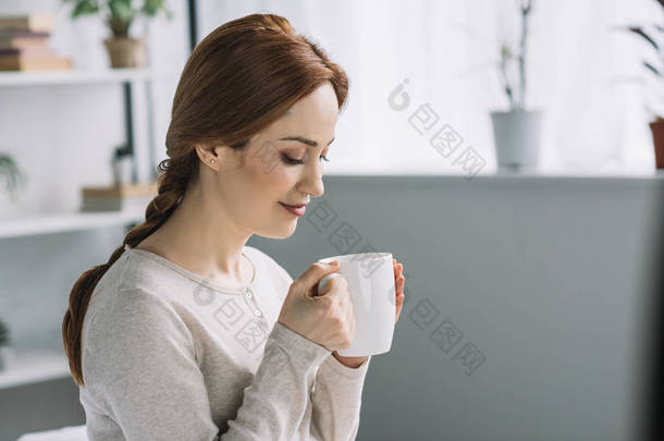美丽的孕妇在家里喝茶的侧面视图
