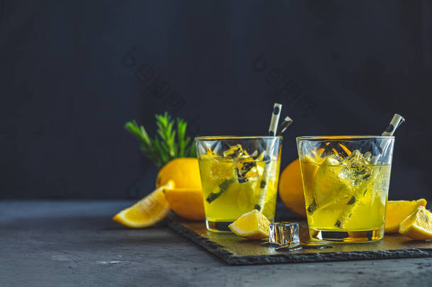柠檬酒精饮料鸡尾酒与冰, 柠檬和迷迭香草本植物在黑色的石头混凝土表面。传统的意大利自制柠檬酒精饮料利口酒利蒙切洛.