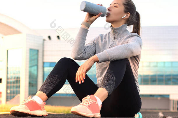 美丽的年轻女子穿着运动服在运动运动后在体育场户外运动喝<strong>水</strong>