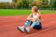 健身女子跑步者坐在跑道上跑步后休息