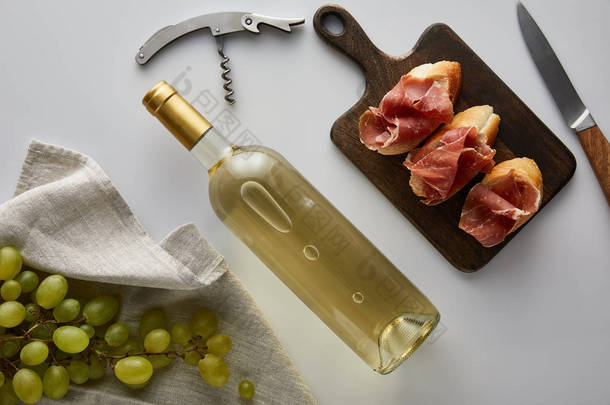 葡萄酒、软木塞、小刀、切碎的意大利面包和白底面包旁边的白葡萄酒瓶盖