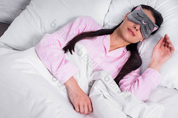 穿粉红色睡衣和睡面具的女人在家里睡觉的画像