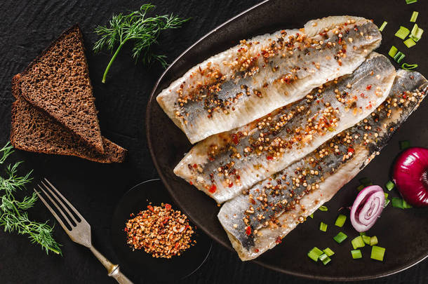 用<strong>调料</strong>、青菜和面包片包裹在深色石质背景上的腌制鱼片或鱼片鲱鱼。地中海食物，开胃菜，海鲜，顶级风景