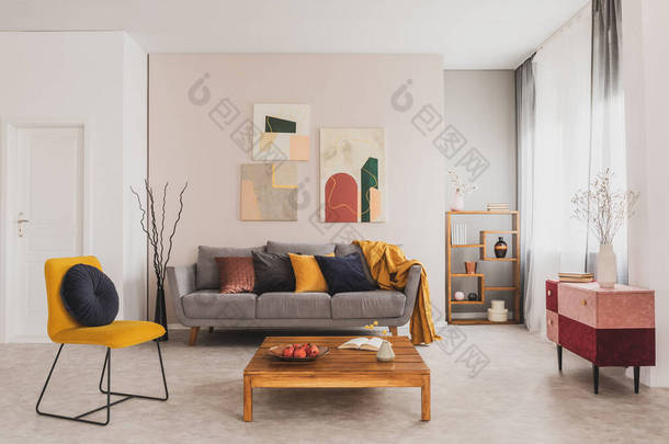 灰色沙发前的木制咖啡桌和黄色椅子，在时髦的客厅里有枕头