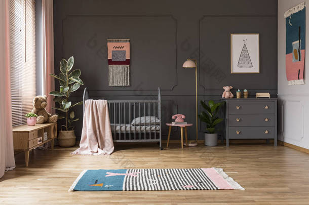 真实照片的婴儿婴儿床在一个灰色的孩子的房间内, 旁边的橱柜, 灯和植物