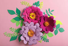 纸五颜六色的花和绿叶在粉红色的背景的顶部看法 