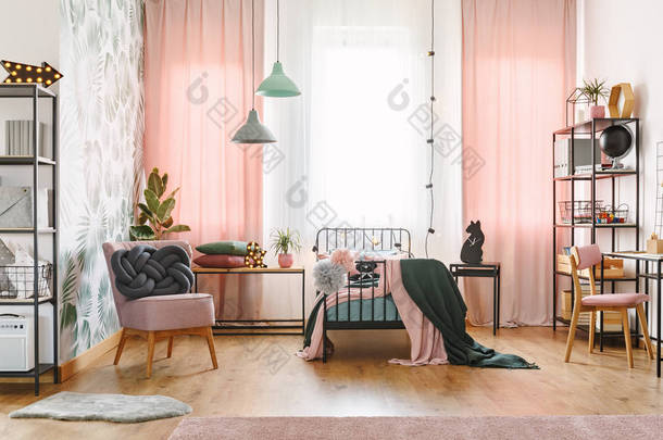 粉红色扶手椅上的结枕在柔和的女孩的卧室内部与灯具和窗帘