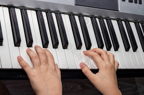 紧紧抓住婴儿弹钢琴的手。 一个玩合成器键盘的孩子的手。 婴儿的手和黑白钢琴键的特写图像.