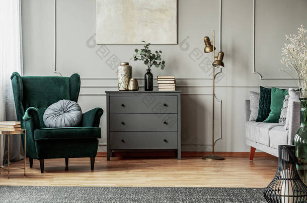 灰色墙壁上的抽象绘画 o 当代客厅内部，带圆形枕头、康模和沙发的翡翠绿色扶手椅