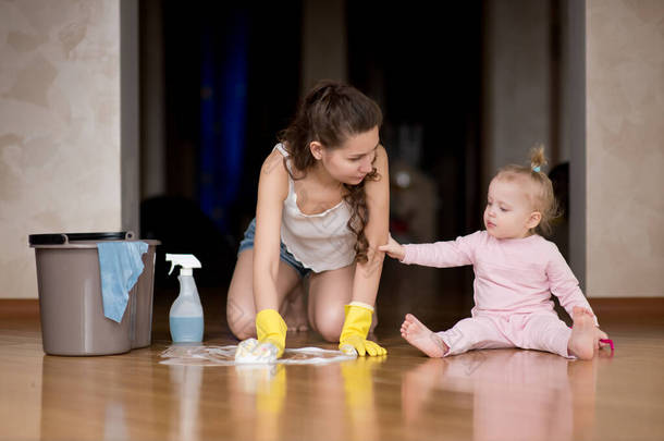 一个小女孩看着她的母亲在她身后扫地。在家里的<strong>走廊</strong>里，女人用身边的地板洗手