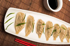 美味的中国水饺放在筷子旁边的盘子里，酱油放在竹席上