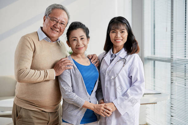高度<strong>专业</strong>的亚洲医生和爱的资深夫妇的小组肖像站立在现代办公室和看在照相机以宽广的微笑
