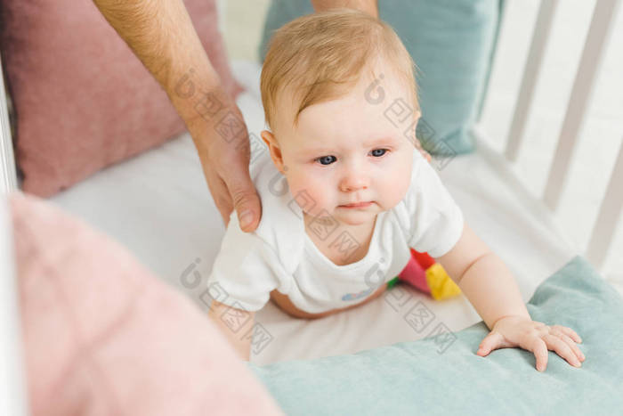 父亲抱婴儿宝宝躺在婴儿床上的裁剪图像