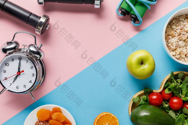 美味的饮食食品和运动器材的顶视图与蓝色和粉红色的背景闹钟 