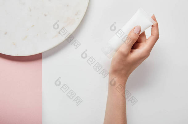 在白色粉红色表面持有奶油管附近的<strong>板</strong>的裁剪视图