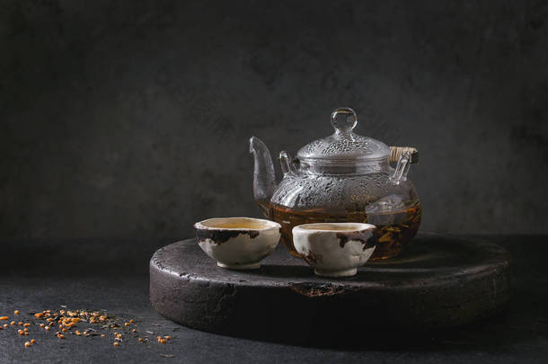 热绿茶在两个传统的中国粘土陶瓷杯和玻璃茶壶站在托盘上的黑色大理石桌子.