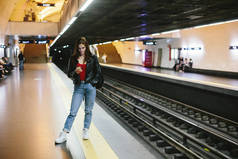 年轻的女临时工在地铁站用手机等火车