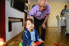 爷爷让孙子坐着玩具车打滚。 外祖父和孙子的重定向。 周末快乐的概念。 爷爷和孙子快乐地走在家里.