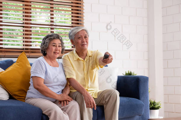 亚洲一对夫妇坐在坐在一个房间里，用<strong>遥控器</strong>换频道，在家里的客厅里看<strong>电视</strong>。.