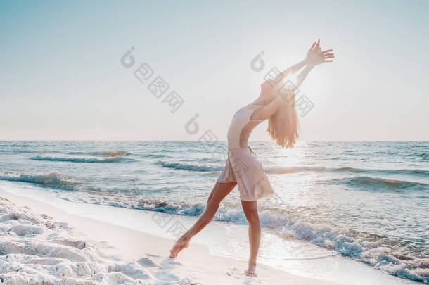苗条美丽的芭蕾舞演员在白色礼服跳舞芭蕾在海上或海洋沙滩上晨光。艺术概念，自然之美