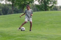 可爱的非洲美国男孩在草地上踢足球 