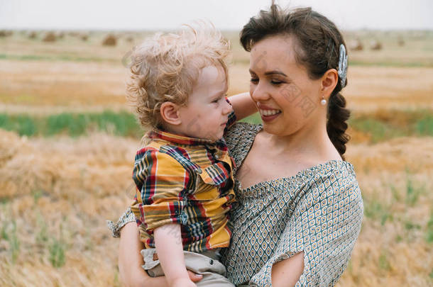 美丽的年轻女子与白发的小儿子在她的怀里，在麦田中间与包在夏夜
