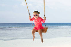 一个快乐的幼儿女孩在树下海滩摇摆的肖像
