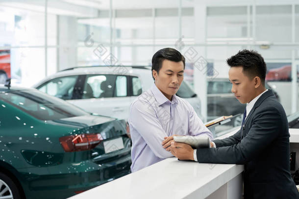 汽车经销商的年轻专业<strong>销售经理</strong>向客户展示平板电脑上的合同细节