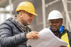 土建工程师, 带着安全帽和黄色夹克, 检查施工现场脚手架中的技术图纸和办公室蓝图