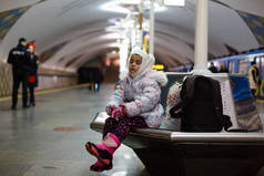 坐在地铁站长椅上穿着保暖衣服的小女孩 