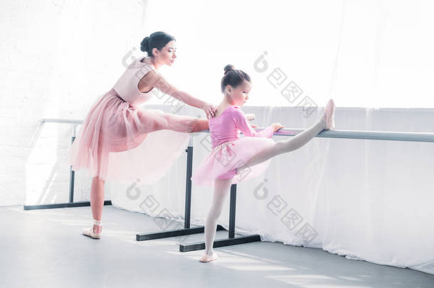 年轻的芭蕾舞老师看着小学生<strong>伸展</strong>芭蕾工作室