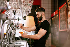 酒保在酒吧酒吧工作英俊的男子倒在玻璃杯啤酒。高分辨率.