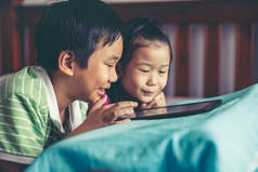 中国男孩和他漂亮的妹妹笑着躺在床上容易。亚洲儿童一起玩数码片游戏。对兄弟姐妹的爱的概念。老式胶片过滤效果.