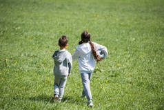 后视图的妹妹和兄弟走在草地上的球 