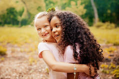 两个快乐的女孩，像朋友一样拥抱彼此在欢快的方式。在公园的小女朋友.