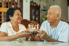 亚洲高级夫妇抱着一个蛋糕，在客厅里微笑