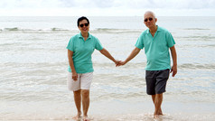亚洲高级夫妇一起在沙滩上漫步于海边