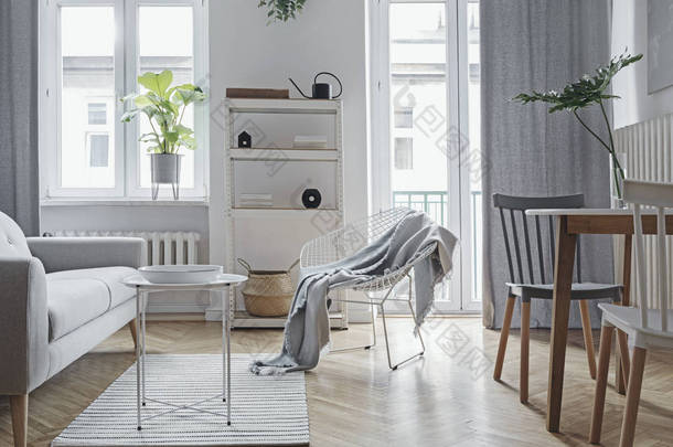 明亮的家庭北欧客厅与设计式的桌子，家庭表，植物，白色书架在墙上。棕色木制镶木地板。白墙上的<strong>抽象</strong>绘画。简约内饰的概念.