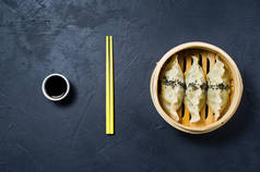 韩国饺子在传统的蒸笼里, 黄色筷子。黑暗背景, 顶部视图