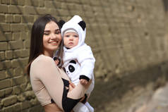 穿着熊猫服装的妈妈怀里的婴儿。一个有孩子的年轻女孩在城市. 