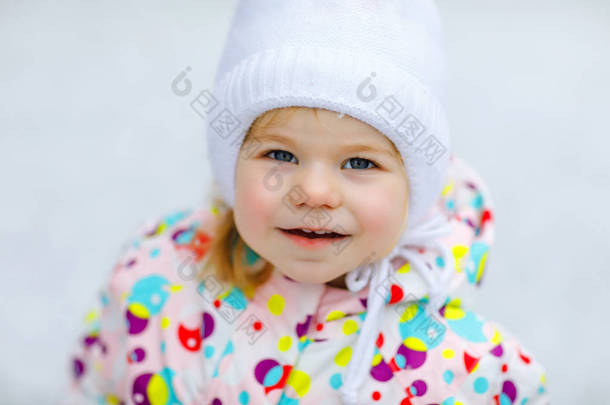 冬天在户外散步的小女孩的画像。可爱的幼儿吃甜棒棒糖.孩子们在寒冷的雪天玩得很开心.穿着温暖的婴儿色彩艳丽的衣服，头戴有泡泡的帽子.