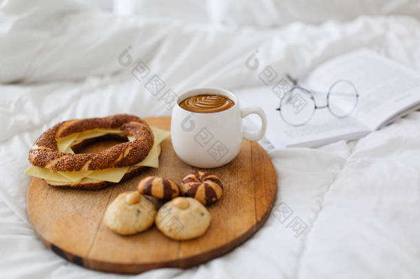 在床上的木托盘上盛放奶酪、自制饼干和咖啡的面包包