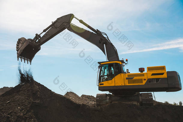 煤矿里的黄色大挖掘机，负载着该品种，背衬着明亮的阳光和美丽的蓝天。矿用卡车采矿机械。煤矿技术