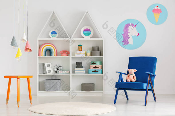 <strong>毛绒玩具</strong>在蓝色扶手椅和五颜六色的吊灯上面橙色桌与蜡笔腿在一个可爱的儿童卧室内部