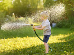 在阳光明媚的后院玩花园软管的滑稽小男孩。学前儿童玩喷雾水的乐趣。儿童夏季户外活动.